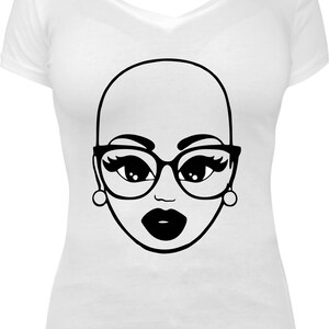 May include: White V-neck t-shirt featuring a black and white graphic of a bald woman's face wearing glasses and earrings. The graphic has large eyes, thick-rimmed glasses, and full lips. The design is simple and bold.
