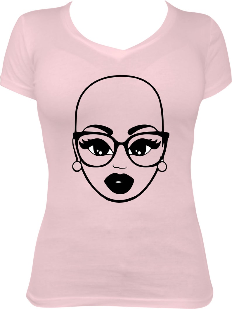 May include: A light pink V-neck t-shirt featuring a black and white graphic of a bald face wearing glasses, earrings, and dark lipstick. The graphic is centered on the front of the shirt.