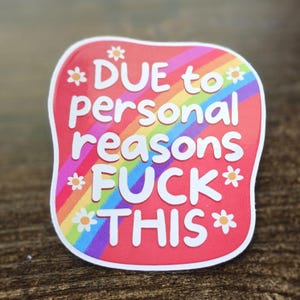 May include: A sticker with a red background and a rainbow design. The sticker has white text that reads "DUE to personal reasons FUCK THIS" with daisy accents. The sticker is on a wooden surface.