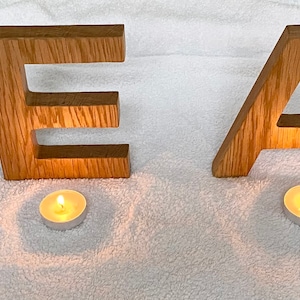 May include: Wooden letters spelling the word "HEAL" are arranged on a white surface. Four small, lit candles are placed in front of each letter.