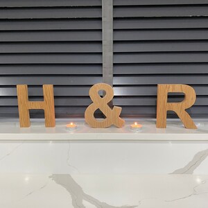 May include: Wooden letters spelling "H & R" with two small candles in front of them on a white countertop.