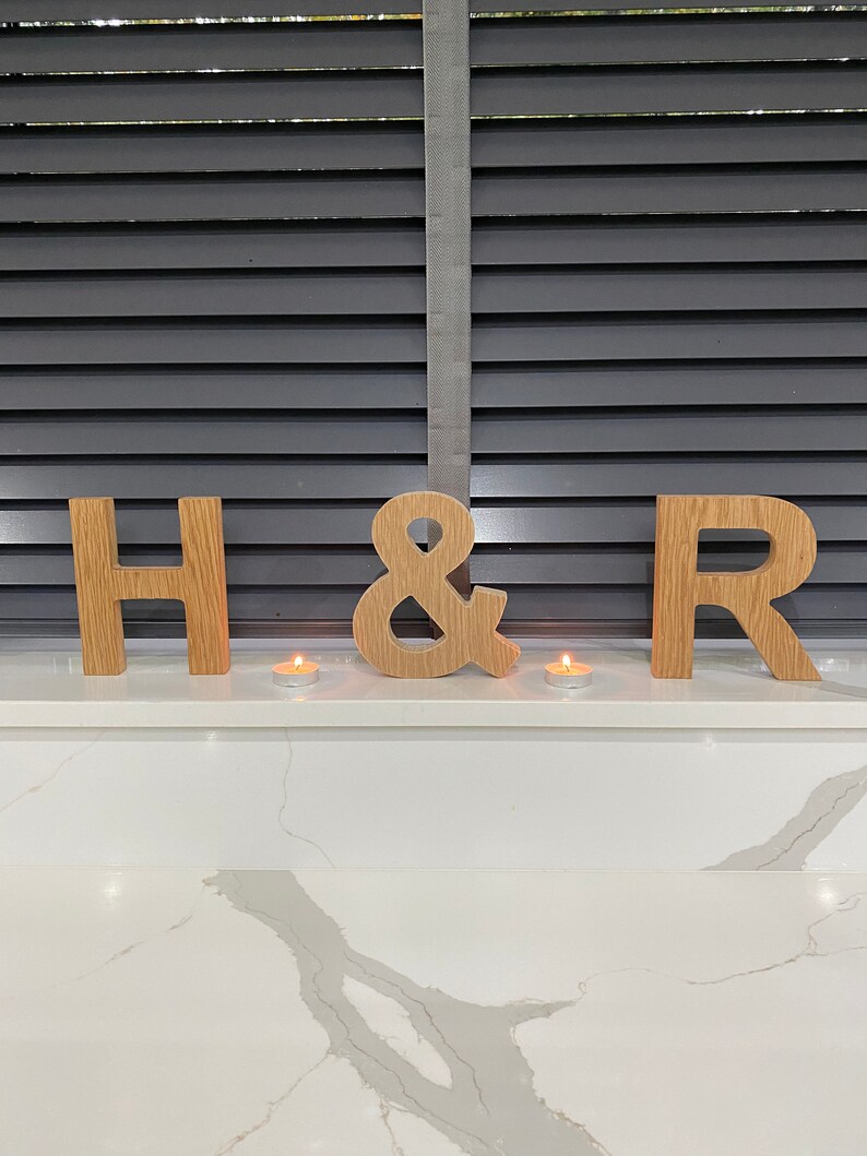 May include: Wooden letters spelling "H & R" with two small candles in front of them on a white countertop.