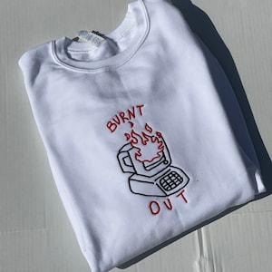 May include: White sweatshirt with a black and red embroidered design of a computer on fire with the text "BURNT OUT".