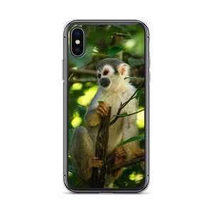 May include: A brown and gray squirrel monkey sitting on a branch in a lush green rainforest. The monkey is looking to the left of the frame.