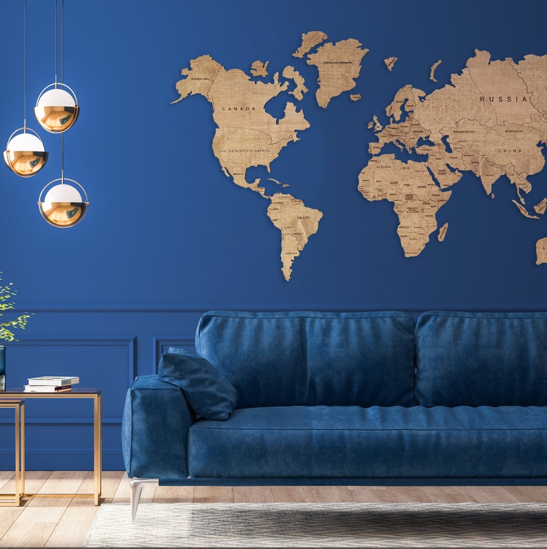 A blue velvet sofa sits in front of a blue wall with a wooden world map hanging above it. Three gold globe-shaped pendant lights hang from the ceiling.