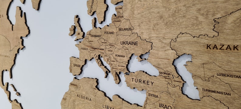 A wooden world map with the countries of Europe, Asia, and Africa labeled. The map is made of light brown wood with dark brown lines outlining the countries. The map is mounted on a white background.