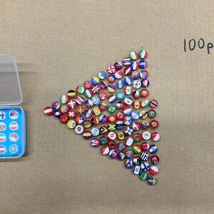 May include: A collection of flag pins, including a clear plastic case with a blue insert holding some pins. The pins are arranged in a triangle shape, with the text "100pcs" written in black marker.