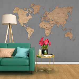 A teal green sofa with two pillows, one with a geometric pattern and one light blue, sits in a living room with a wooden floor. A gold side table with a round top and three legs sits next to the sofa. A vase with pink flowers sits on the table. A wooden world map hangs on the wall behind the sofa.