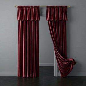 Op de afbeelding: Bordeaux fluwelen gordijnen met bijpassende valletjes, hangend aan een goudkleurige roede. De gordijnen zijn gedrapeerd, met één kant teruggetrokken, waardoor een glimp van het interieur van de kamer te zien is. De stof heeft een zachte glans en voegt een vleugje luxe toe aan de raambekleding.