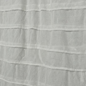 Op de afbeelding: Witte stof met een gelaagd ontwerp. Horizontale lagen worden gescheiden door dunne, witte banden. De semi-transparante stof creëert een gestructureerd, gelaagd effect. De algehele esthetiek is strak en minimalistisch.