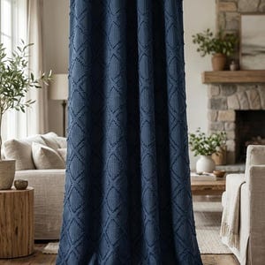 Op de afbeelding: Een marineblauw gordijn met een ruitpatroon hangt aan een metalen stang. De textuurstof valt tot op de vloer en creëert een gezellige en stijlvolle uitstraling. Het gordijn bevindt zich in een woonkamer met een open haard en neutrale meubels.