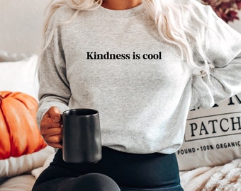 Könnte beinhalten: Ein hellgraues Sweatshirt mit Rundhalsausschnitt und dem schwarzen Schriftzug Kindness is cool auf der Brust. Das Kleidungsstück hat lange Ärmel und einen gerippten Halsausschnitt und bietet einen schlichten Look für den Alltag zu jeder Jahreszeit.
