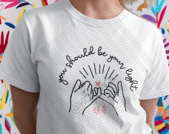 Könnte beinhalten: Weißes T-Shirt mit einer schwarzen Grafik von zwei Händen, die sich mit einem Herzen einen kleinen Finger versprechen, und dem Text "you should be your light".