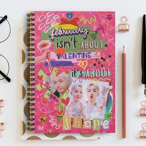 May include: Pink spiral notebook with a collage of images and text. The text reads "february isn't about valentine it's about jhope".