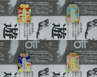 May include: Four gold-colored enamel pins with a Japanese design. Each pin features a different color scheme and a different Japanese character. The pins are all rectangular in shape and have a gold-colored border.