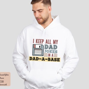 Könnte beinhalten: Weißer Hoodie mit einer Grafik einer Diskette und dem Text "I keep all my dad jokes in a dad-a-base".