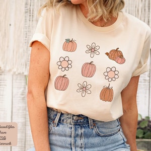Op de afbeelding: Een beige T-shirt met een grafisch ontwerp van roze en oranje pompoenen en witte bloemen.