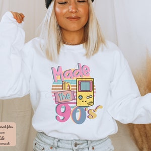 May include: White sweatshirt with a pink, yellow, and blue graphic that says "Made in the 90's" with a retro video game controller.