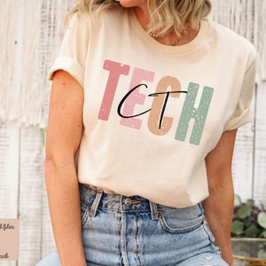 Puede incluir: Una camiseta beige claro con la palabra "TECH" impresa en una fuente desgastada. Las letras son de diferentes colores: rosa, naranja, marrón y verde.