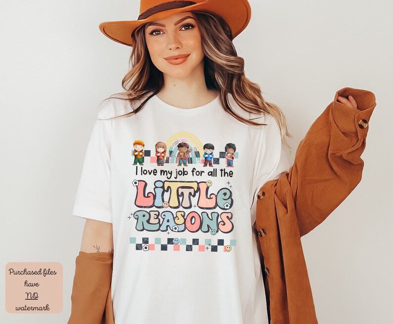 Pu&ograve; includere: Maglietta bianca con una grafica colorata che dice "I love my job for all the little reasons". La grafica presenta un arcobaleno, uno schema a scacchi e bambini dei cartoni animati.
