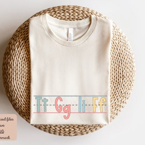 Pu&ograve; includere: Una maglietta beige con una riga di lettere che dice "Tt Gg Li Ff" in lettere colorate e contornate.