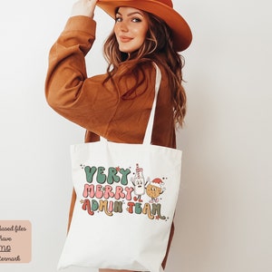 May include: White tote bag with the text "Very Merry Admin Team" in colorful, stylized letters. A cartoon milk carton and cookie with Santa hats are next to the text.