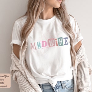 May include: A white t-shirt with the word "MIDWIFE" printed on it in colorful, block letters. The letters are slightly distressed and have a vintage look.