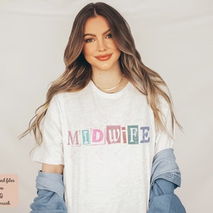 May include: A white t-shirt with the word "MIDWIFE" printed in colorful, block letters. The letters are in different colors, including pink, blue, green, and yellow.