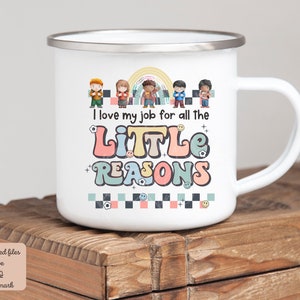 Pu&ograve; includere: Tazza di smalto bianco con un design colorato che presenta un arcobaleno, bambini e il testo "Adoro il mio lavoro per tutte le piccole ragioni".