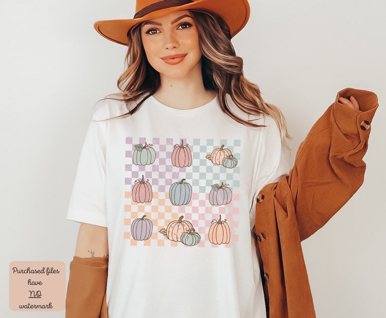 May include: A white t-shirt featuring a colourful checkered pattern and a design of pastel pumpkins. The pumpkins are arranged in a grid pattern on the shirt.