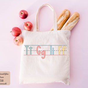 Pu&ograve; includere: Una borsa di tela bianca con le lettere "Tt Gg Ii Ff" scritte a mano in colori. La borsa &egrave; circondata da mele rosse e due pagnotte di pane.