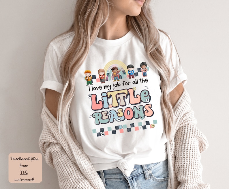 Pu&ograve; includere: Maglietta bianca con una grafica colorata che dice "I love my job for all the little reasons". La grafica presenta un arcobaleno, un gruppo di bambini e uno schema a scacchi.