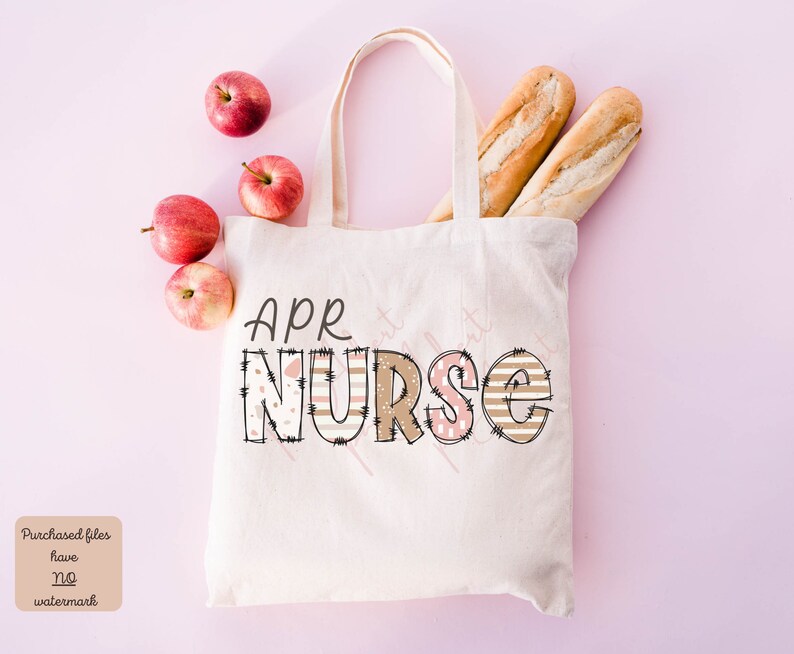 May include: A white canvas tote bag featuring the text "APR NURSE" in brown and pink patterned letters. The bag is displayed against a pink background with apples and bread.