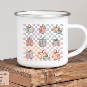 May include: White enamel mug with a checkered pattern and a repeated design of pastel coloured pumpkins. The mug has a white handle.