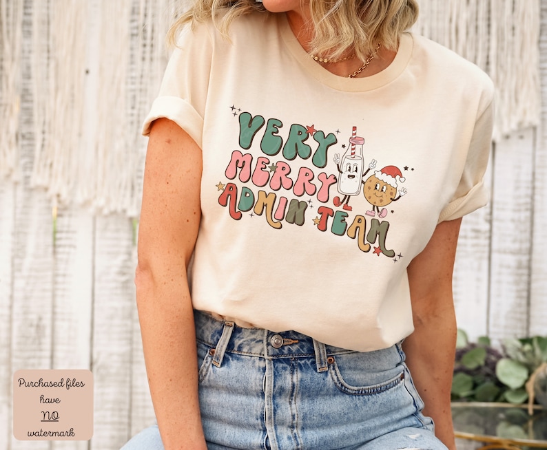 May include: A cream colored t-shirt with a retro design featuring a milk carton and a cookie wearing a Santa hat. The text on the shirt reads "Very Merry Admin Team".