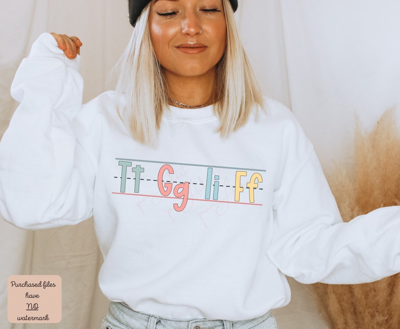 Pu&ograve; includere: Felpa bianca con una grafica delle lettere "Tt Gg Li Ff" scritte in uno stile calligrafico colorato su uno sfondo rigato.