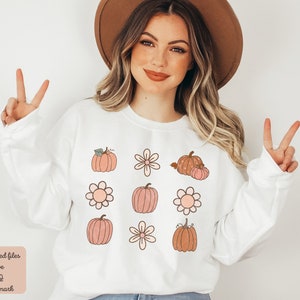 Op de afbeelding: Witte trui met een patroon van roze en bruine pompoenen en witte bloemen. De tekst "Purchased files have no watermark" staat onderaan de afbeelding.