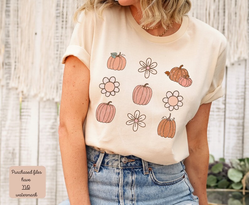 Op de afbeelding: Een beige T-shirt met een grafisch ontwerp van roze en oranje pompoenen en witte bloemen.