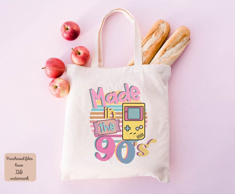 May include: A white canvas tote bag with a retro design featuring the text "Made in the 90's" in pink, yellow, and blue. A yellow and green pixelated video game console is featured on the bag.