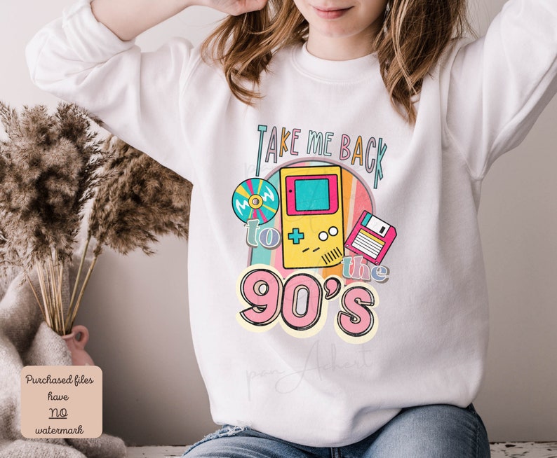 K&ouml;nnte beinhalten: Wei&szlig;er Pullover mit einem Grafikdesign, das eine Retro-Videospielkonsole, eine Diskette und eine CD zeigt. Der Text "Take Me Back to the 90's" ist in einer bunten Schrift gedruckt.
