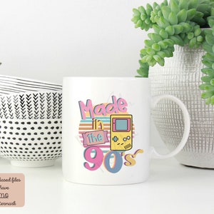 May include: White ceramic mug with a graphic design that says "Made in the 90's" with a retro-style video game controller.