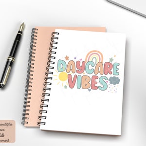 May include: Two spiral-bound notebooks, one peach and one white, with a black pen. The white notebook features the text "DAYCARE VIBES" in colorful bubble letters, with a rainbow, sun, and stars graphic. The notebooks are on a white surface.