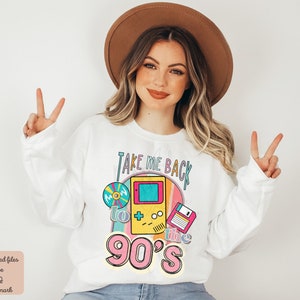 K&ouml;nnte beinhalten: Wei&szlig;er Pullover mit einem Grafikdruck eines Retro-Videospiels, einer Diskette und einer Schallplatte. Der Text auf der Grafik lautet "Take Me Back to the 90's".