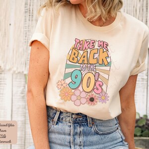 May include: A beige t-shirt with a graphic print that says "Take Me Back to the 90's" in colorful retro font with a sunburst design and flowers.