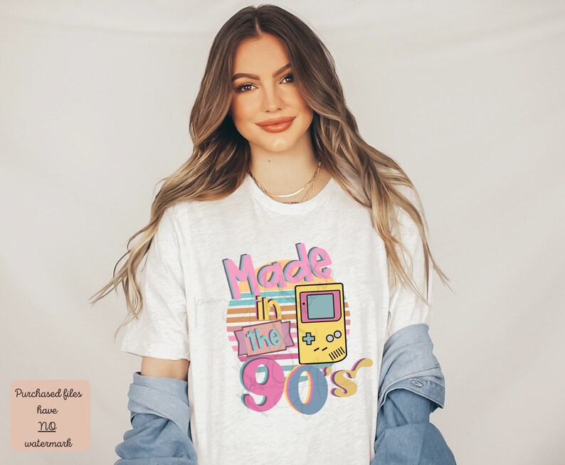 May include: White t-shirt with a graphic design that says "Made in the 90's" with a retro video game console illustration.