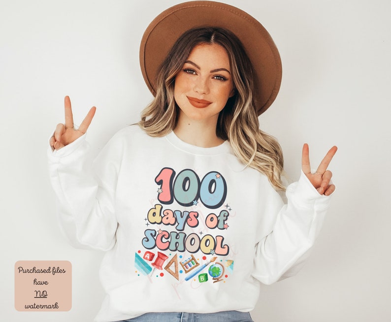 K&ouml;nnte beinhalten: Wei&szlig;er Pullover mit einer bunten Grafik, auf der "100 Tage Schule" steht, umgeben von Schulutensilien.