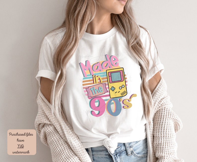 May include: White t-shirt with a graphic design that says "Made in the 90's" with a retro video game controller graphic.