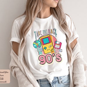 K&ouml;nnte beinhalten: Wei&szlig;es T-Shirt mit einem Grafikdesign, das "Take Me Back to the 90's" mit einem Retro-Videospiel, einer Diskette und einer CD sagt.