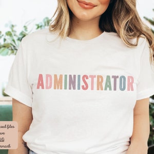 May include: A white t-shirt with the word "ADMINISTRATOR" printed in rainbow colors. The letters are slightly faded and have a textured look.