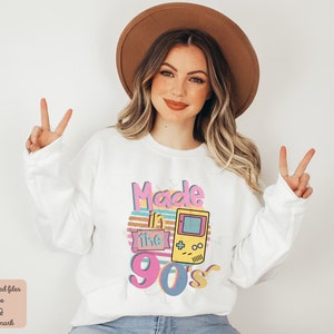 May include: White sweatshirt with a graphic design that says "Made in the 90's" with a retro video game console graphic.